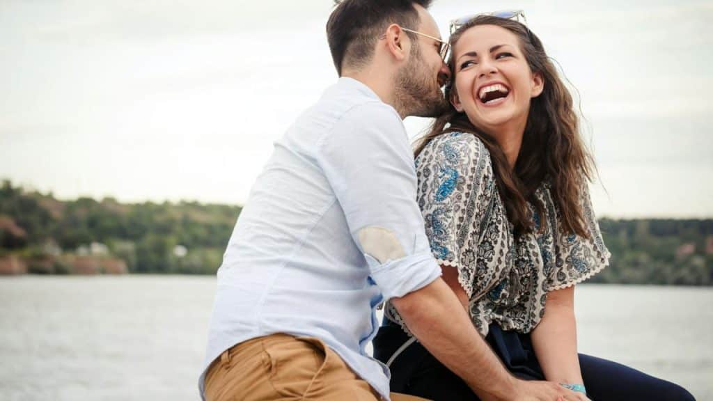 A couple laughing together while sitting outdoors near the water.