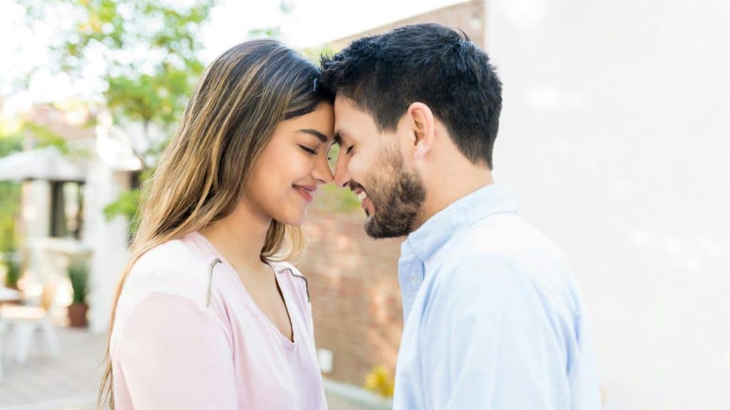 A couple standing close together with their foreheads touching and smiling.