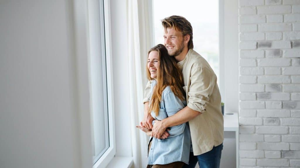 A happy couple standing by a window and embracing each other.
