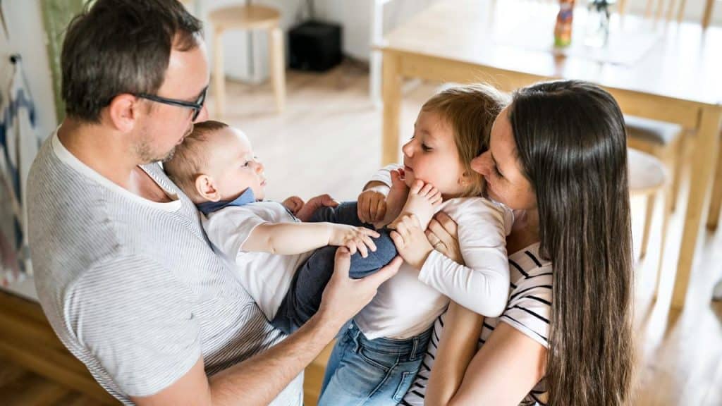 A family at home with parents holding their two young children.