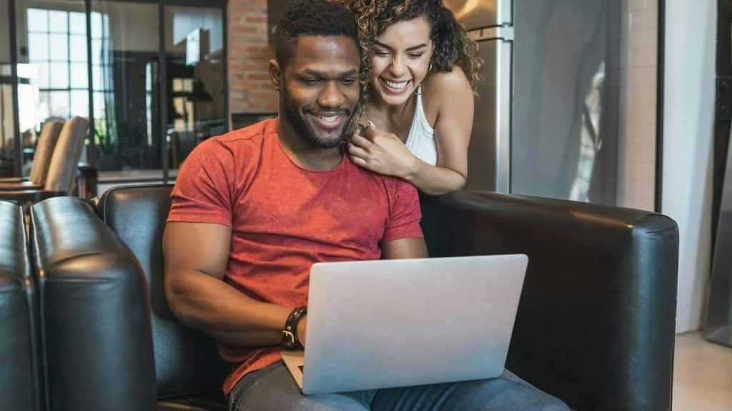 A smiling couple sitting together and looking at a laptop.