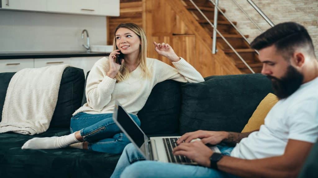 A man using his laptop while his wife talks on the phone