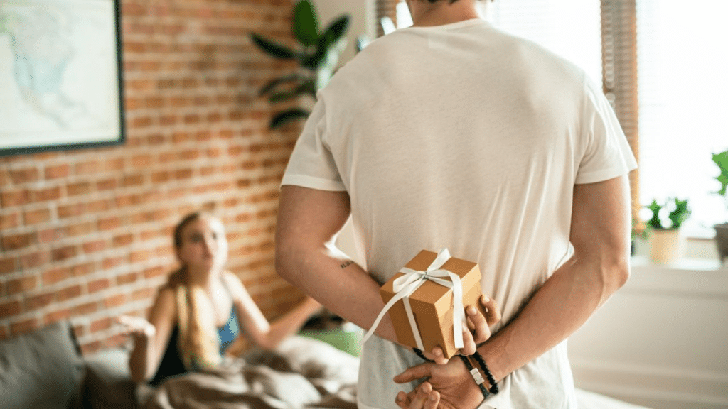 A man holds a wrapped gift behind his back, facing a frustrated woman.