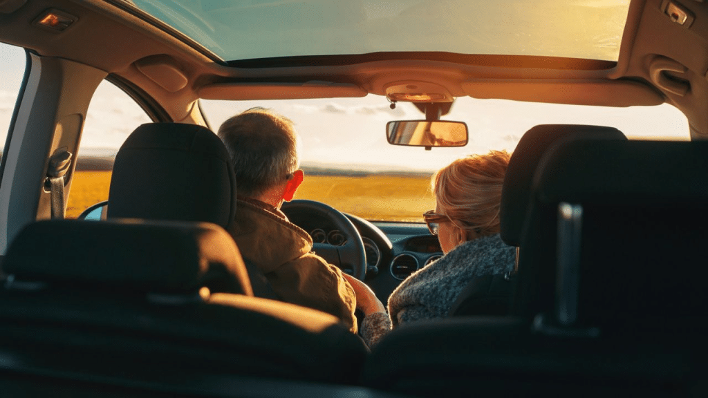 A man and a woman in a car look out at a field during sunset.