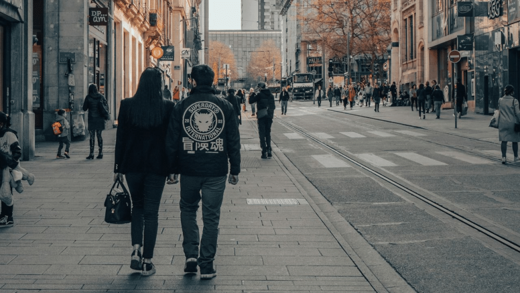 A man and woman walk down a city street, seen from behind.