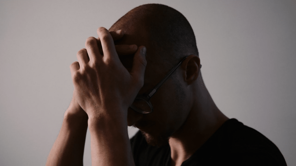 A stressed man holds his head in his hands. He has glasses on, and his face is turned away from the camera.