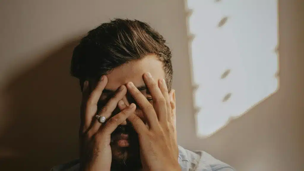 A man covering his face with his hands in a dimly lit room.