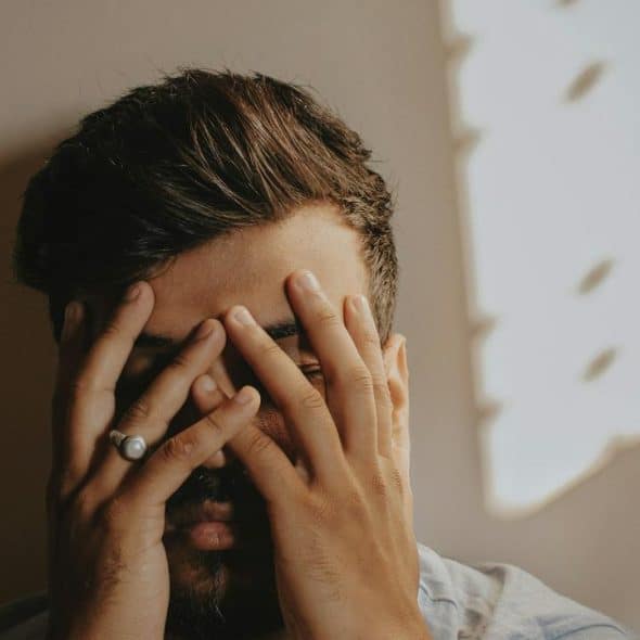 A man covering his face with his hands in a dimly lit room.