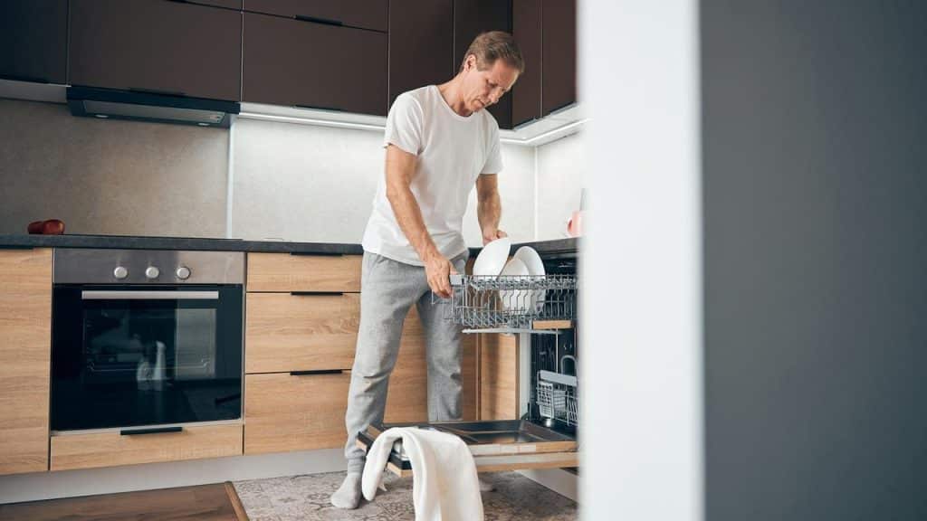 A man unloading clean dishes from a dishwasher in a kitchen.