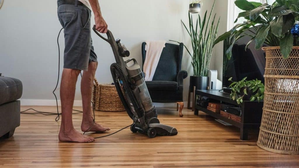 A person vacuuming the wooden floor in a living room.