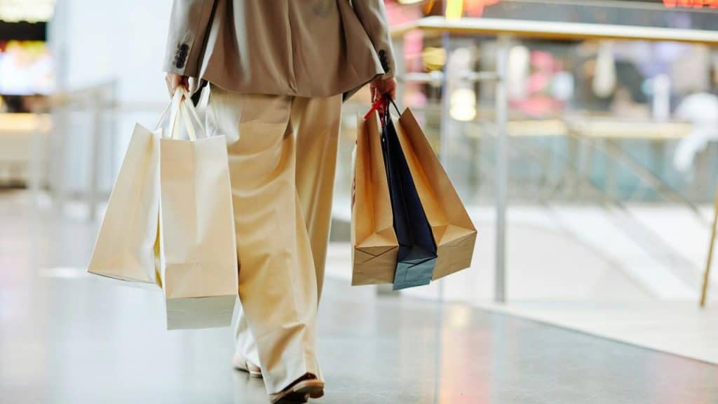 A person walks indoors carrying several shopping bags in both hands.