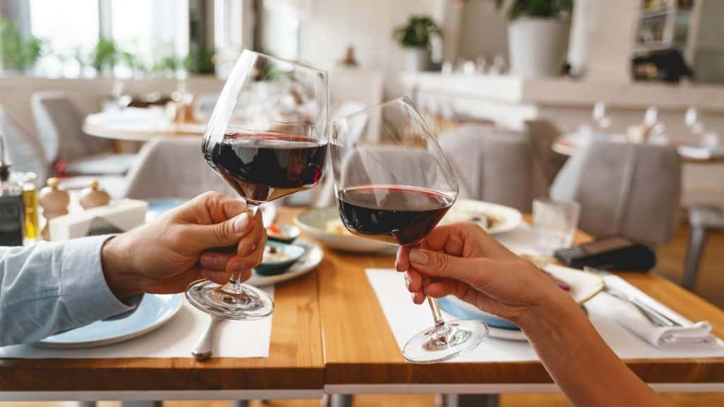 A pair of hands clink glasses of red wine at a restaurant table.