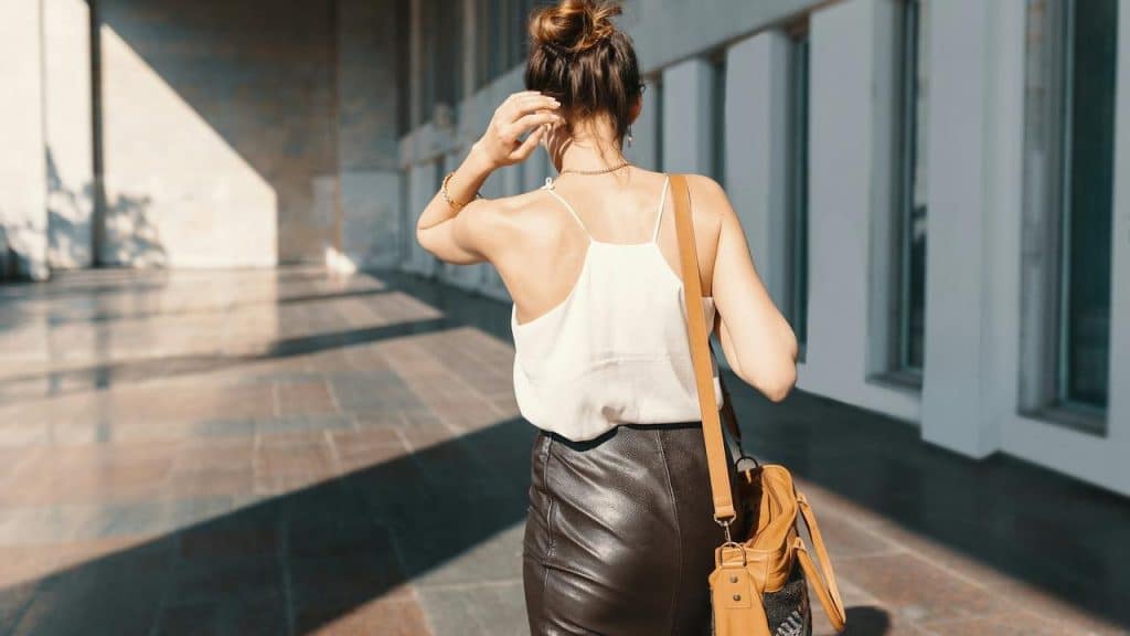 A woman with a bun and shoulder bag walks through a sunlit hallway.