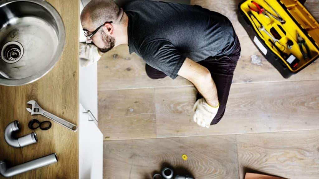 A man with tools near a sink looking overwhelmed