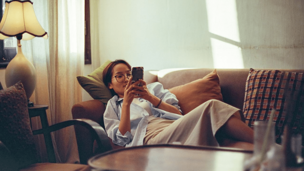 A woman in glasses lies on a couch and looks at her phone.