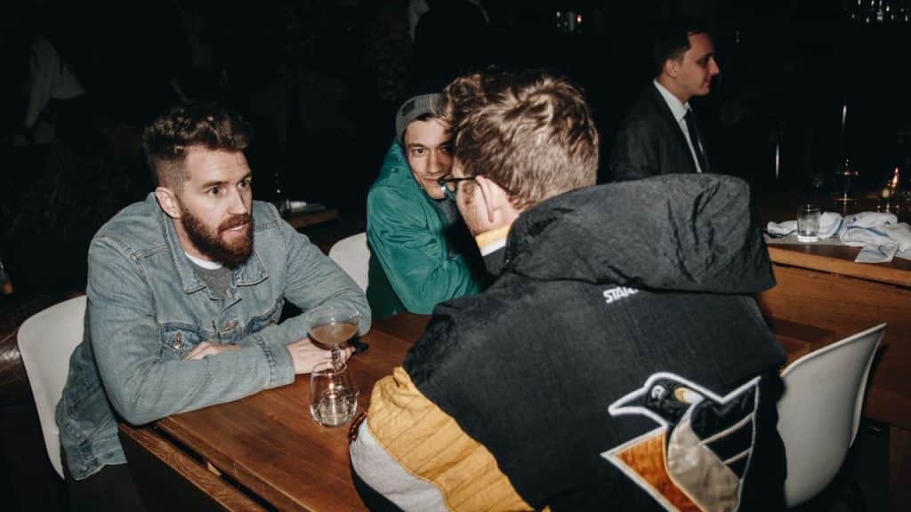 Three men sit at a dark wooden table in a bar or restaurant.