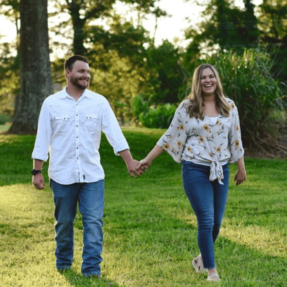 A happy couple holding hands and walking together in a grassy field.