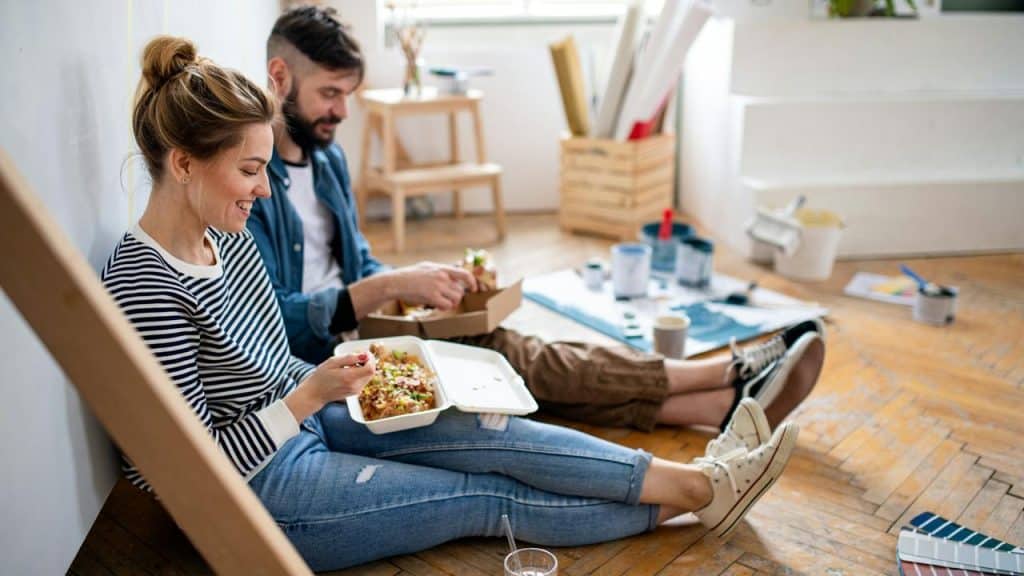 A couple sitting on the floor eating takeout food.