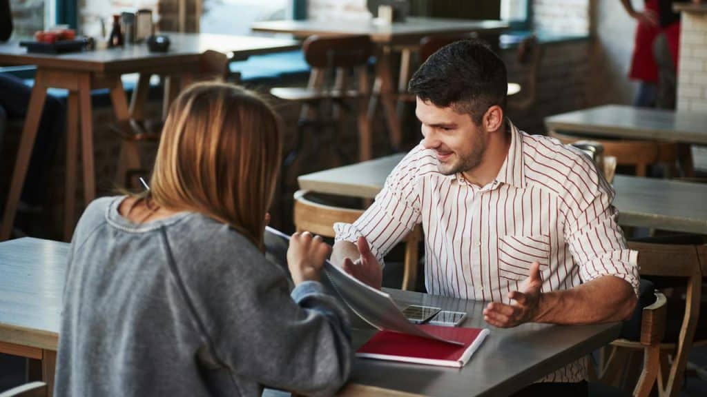 A man and woman having a discussion at a café table with notebooks.