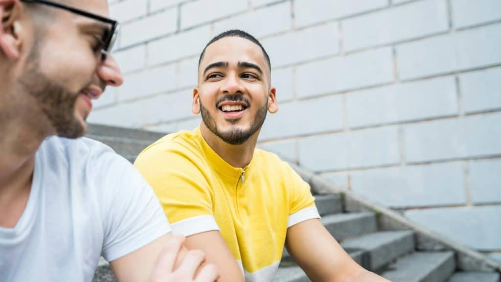 A man in a yellow shirt smiling while talking to a friend.