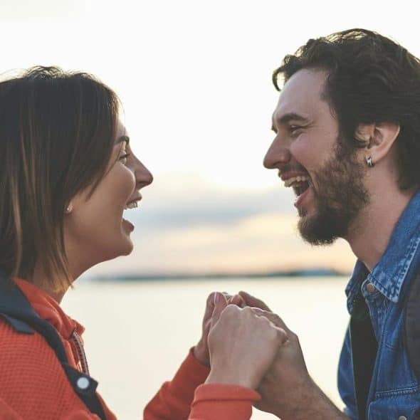 A couple laughing and holding hands outdoors.
