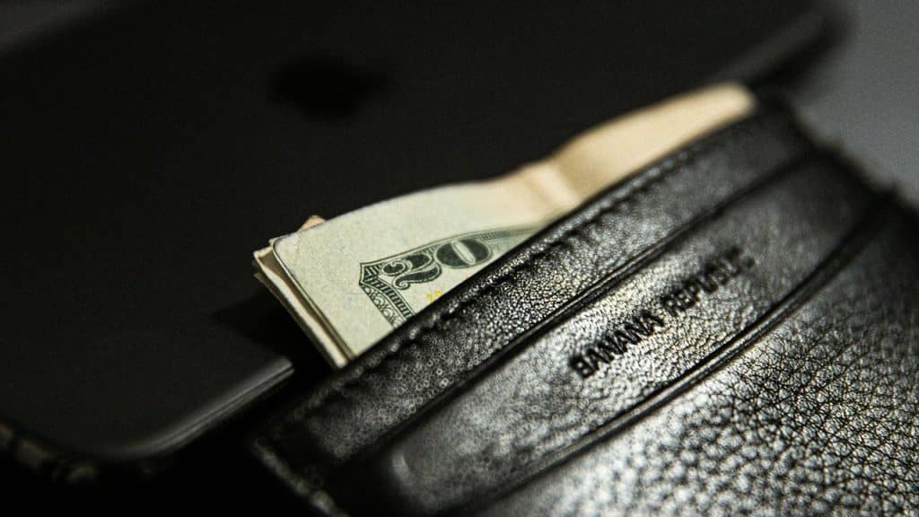 A black leather wallet with cash sticking out placed on top of a phone.
