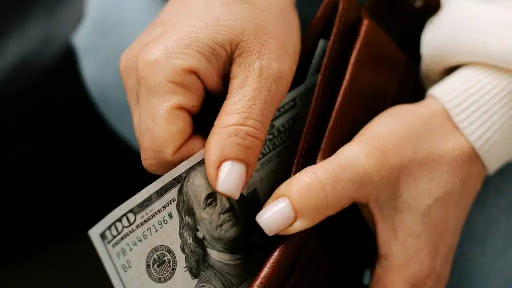 A person taking a hundred-dollar bill out of a brown wallet.