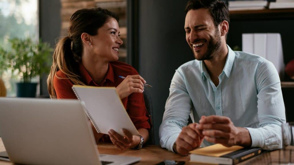 A man and woman smiling and laughing while at a desk.