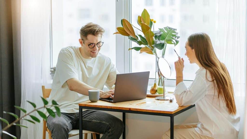 A man working on a laptop at a table while a woman sits across from him.