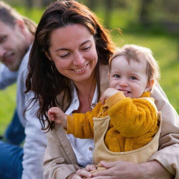 A mother holding her baby while the father sits beside them outdoors.