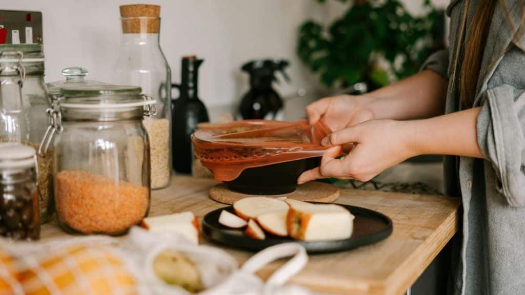 A person covering a bowl with a reusable silicone lid in a kitchen.