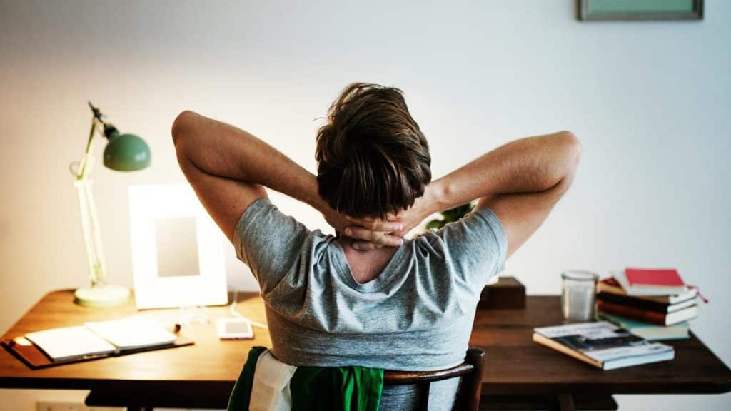 A man sitting at a desk with his hands resting on the back of his neck.