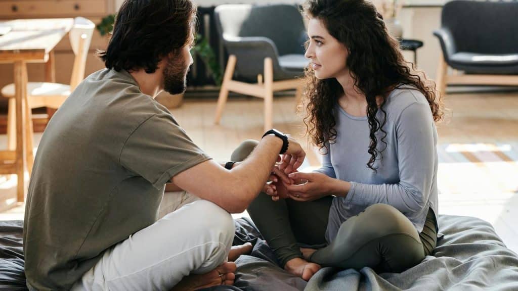 A couple sitting on the floor holding hands and talking seriously.
