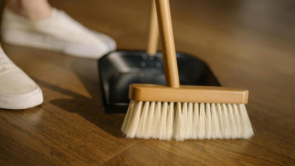 A broom and dustpan being used to clean a wooden floor.