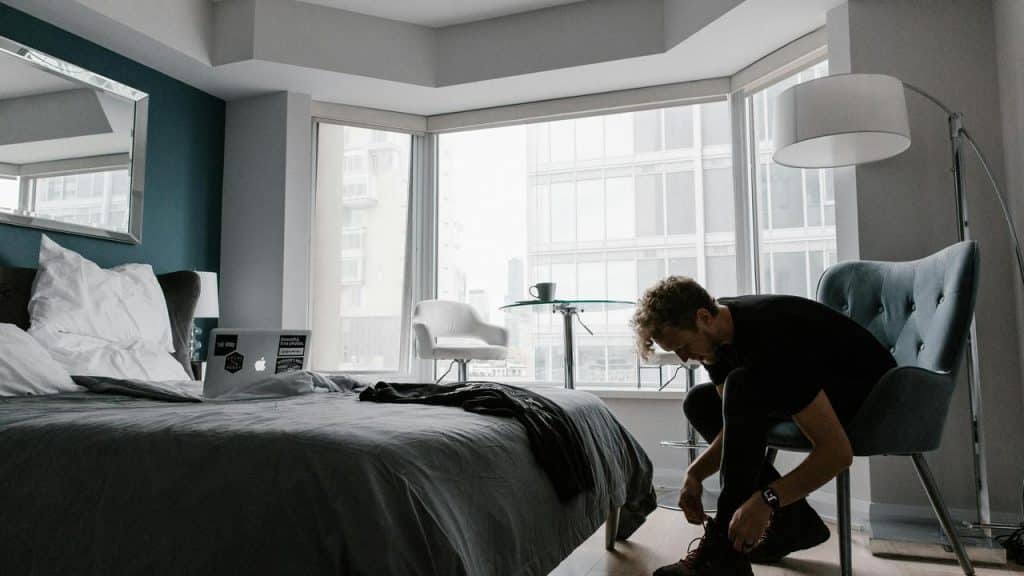 A man sitting in a chair tying his shoes in a modern bedroom.