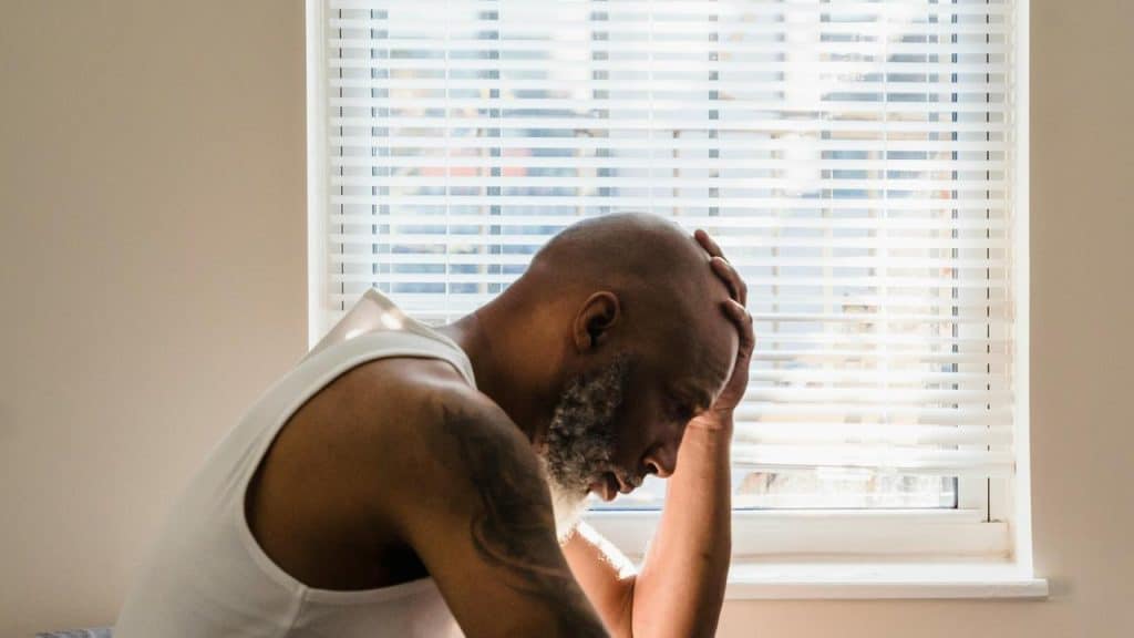 A man sitting by a window with his hand on his head, looking stressed.