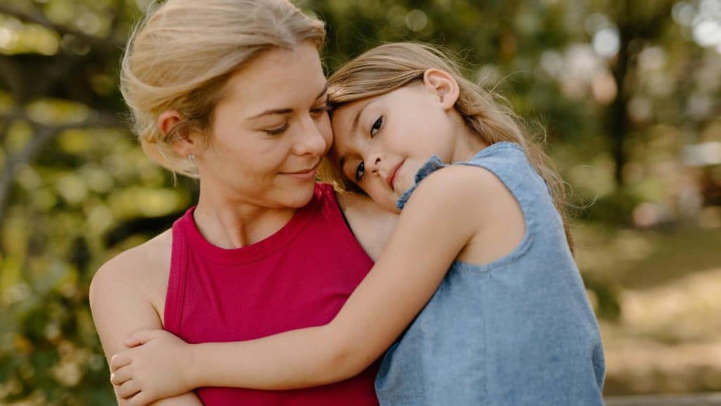 A mother holding her daughter in a tender embrace outdoors.