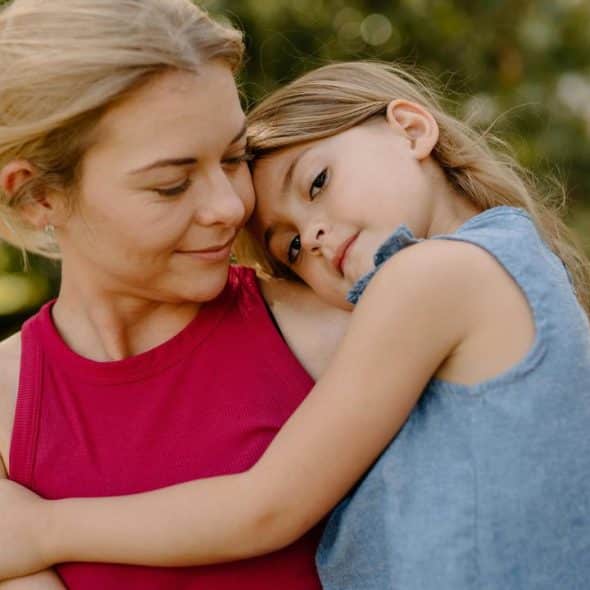A mother holding her daughter in a tender embrace outdoors.