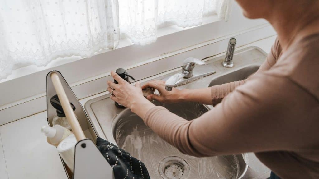 A person washing their hands at a kitchen sink.