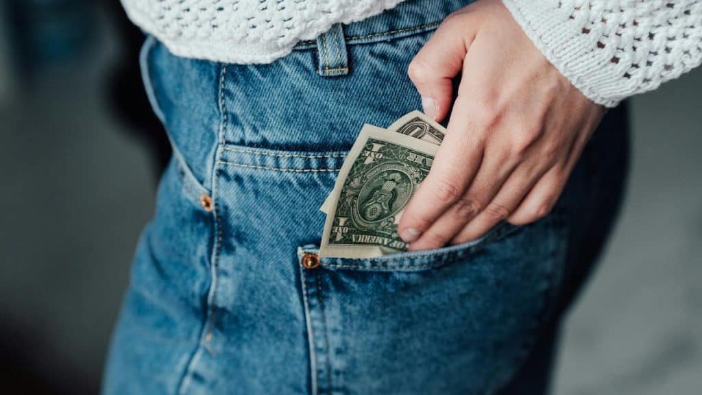 A person putting dollar bills into the back pocket of blue jeans.