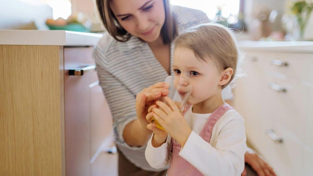 A mother helping her child drink juice from a glass.