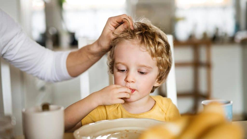 A young boy eating at the table while an adult gently touches his hair.