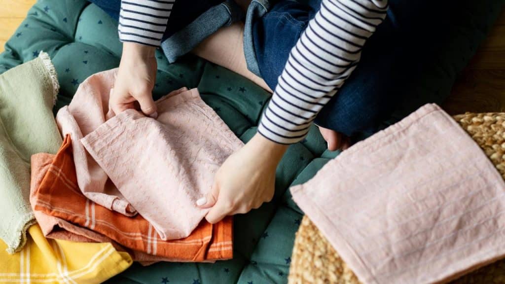 A person folding colorful cloth napkins while sitting on the floor.