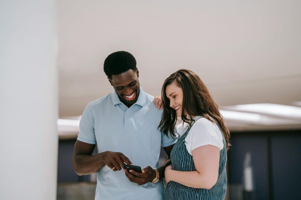 A man and woman laughing at something on phone