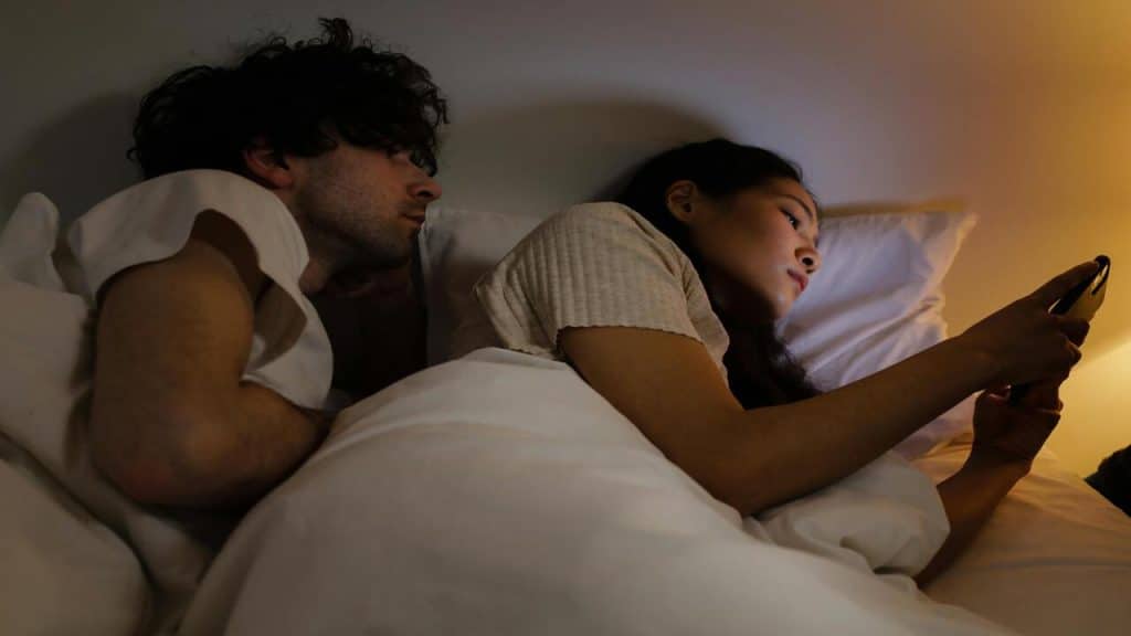 A woman texting at night while her husband discreetly looks