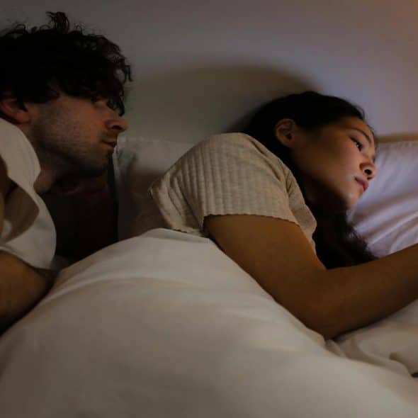 A woman texting at night while her husband discreetly looks