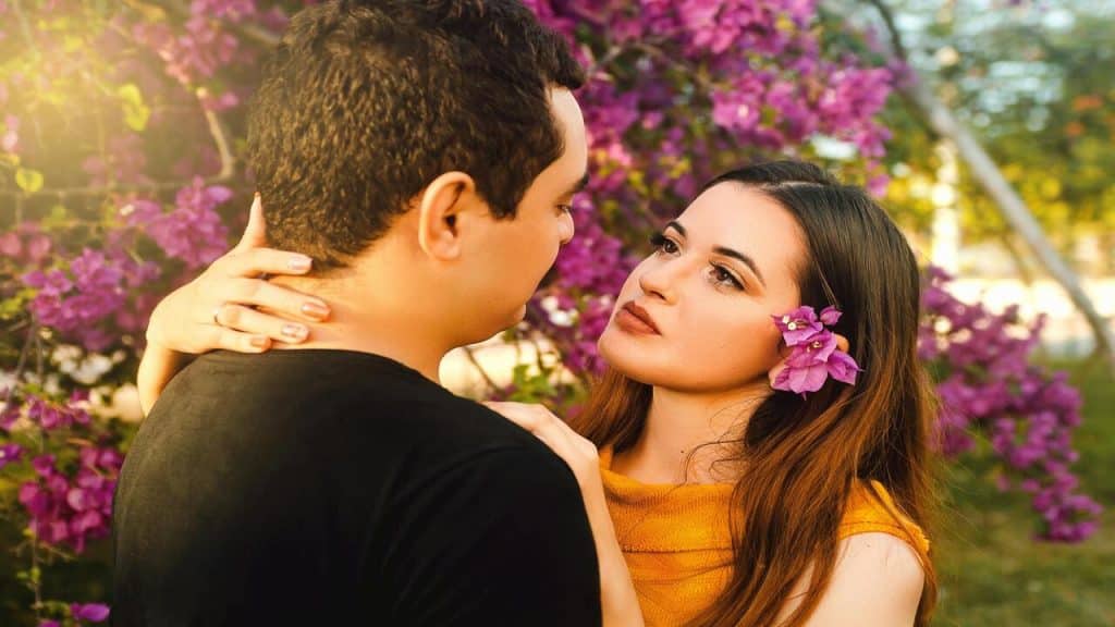 A couple looking at each other beside some flowers