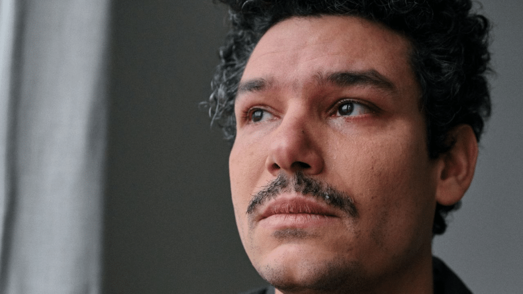 A sad man with a mustache and curly hair looks into the distance, with tears in his eyes.