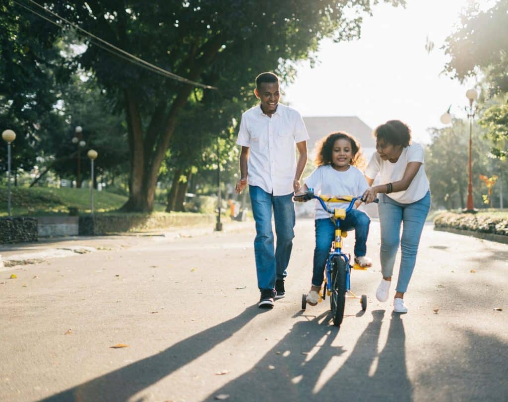 A man and woman teaching their child to ride a bike