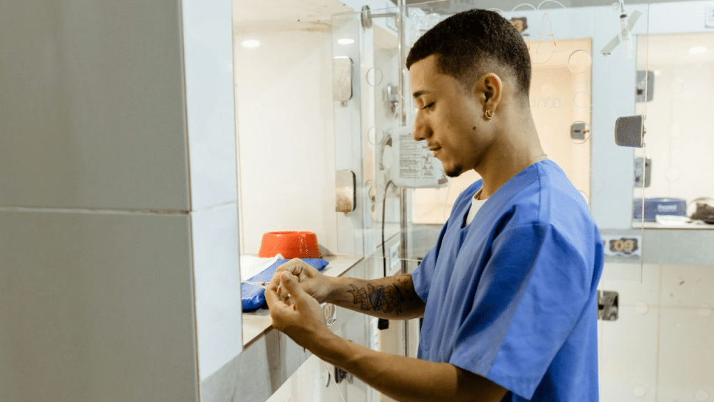 A person in blue scrubs is standing inside what looks like an animal clinic, holding something small in his hands.